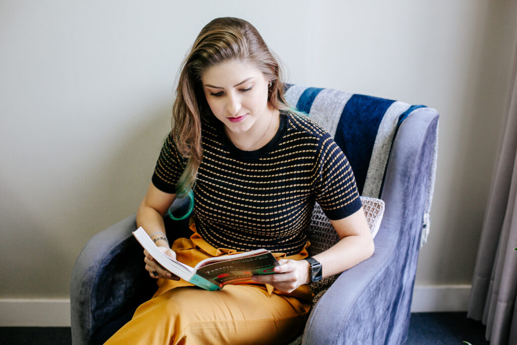 Psicóloga Joice sentada em uma poltrona, realizando a leitura do livro "Terapia Cognitivo-Comportamental - Teoria e prática"